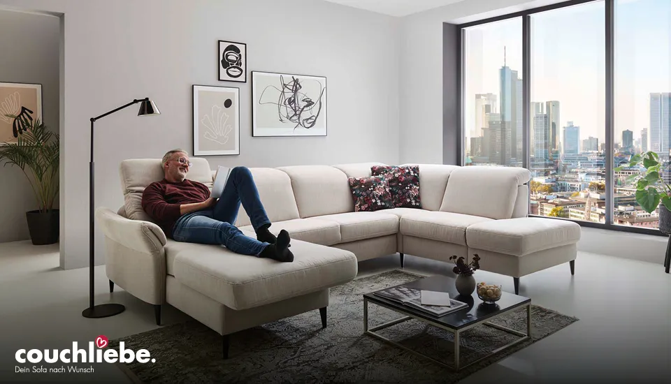 Großes beiges Ecksofa von Couchliebe in modernem Wohnzimmer mit großem Panoramafenster und Stadtblick, komfortable Sitzfläche und Dekokissen sorgen für zeitgemäßes, gemütliches Wohnambiente.
